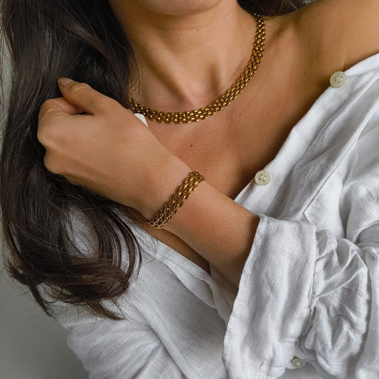 Person wearing a gold chain necklace and bracelet, with a white shirt.