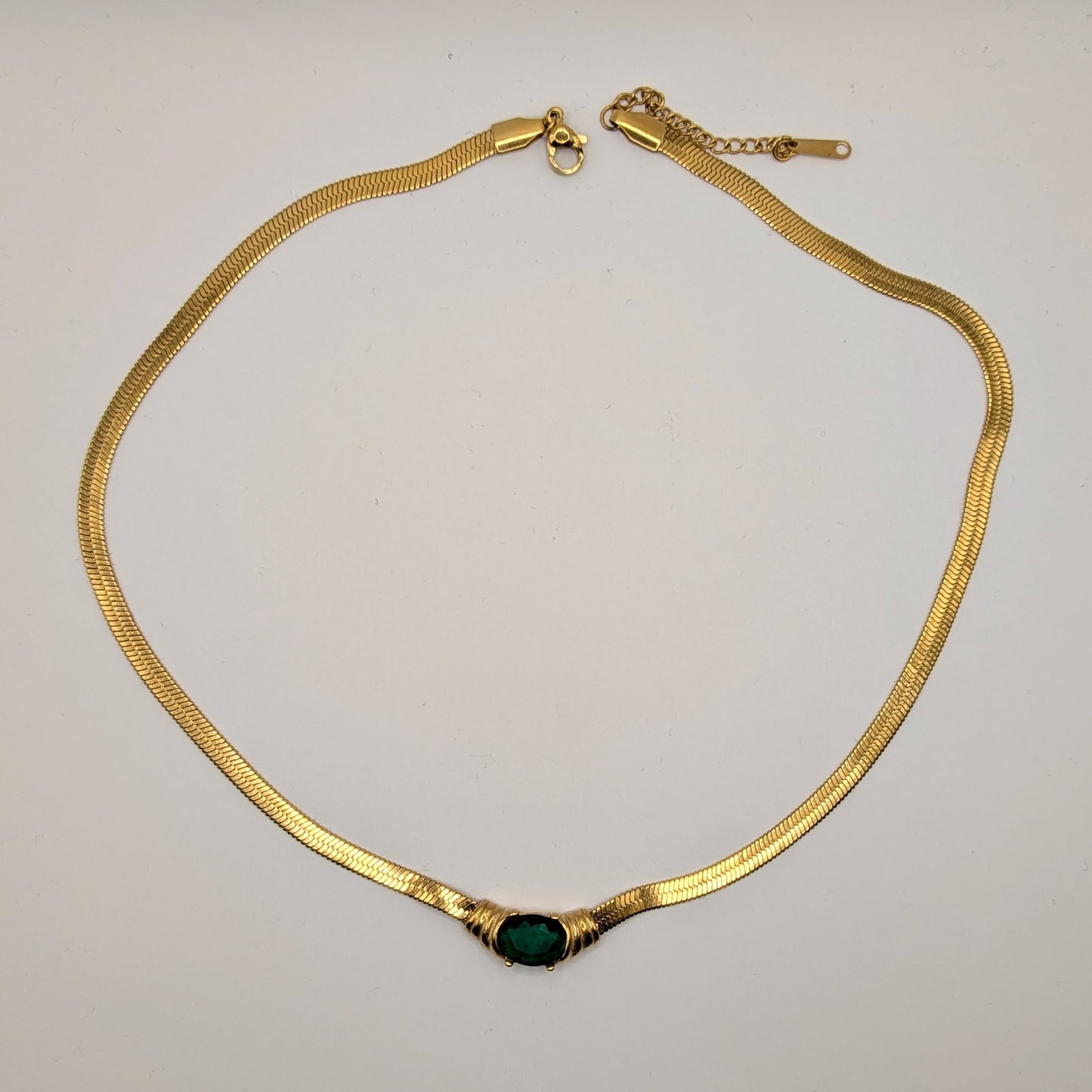 Gold necklace with a green gemstone on a light gray background