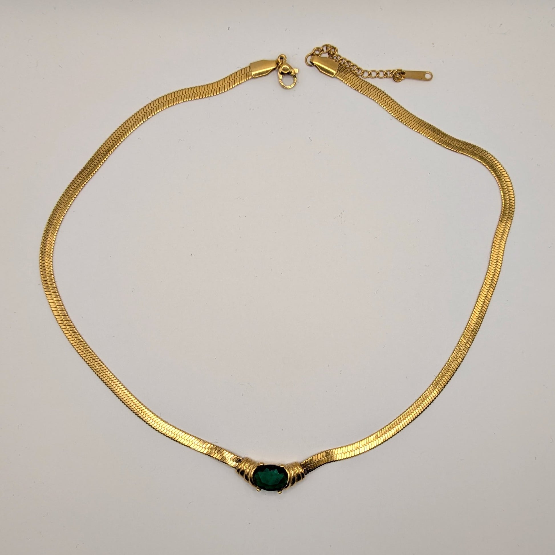Gold necklace with a green gemstone on a light gray background