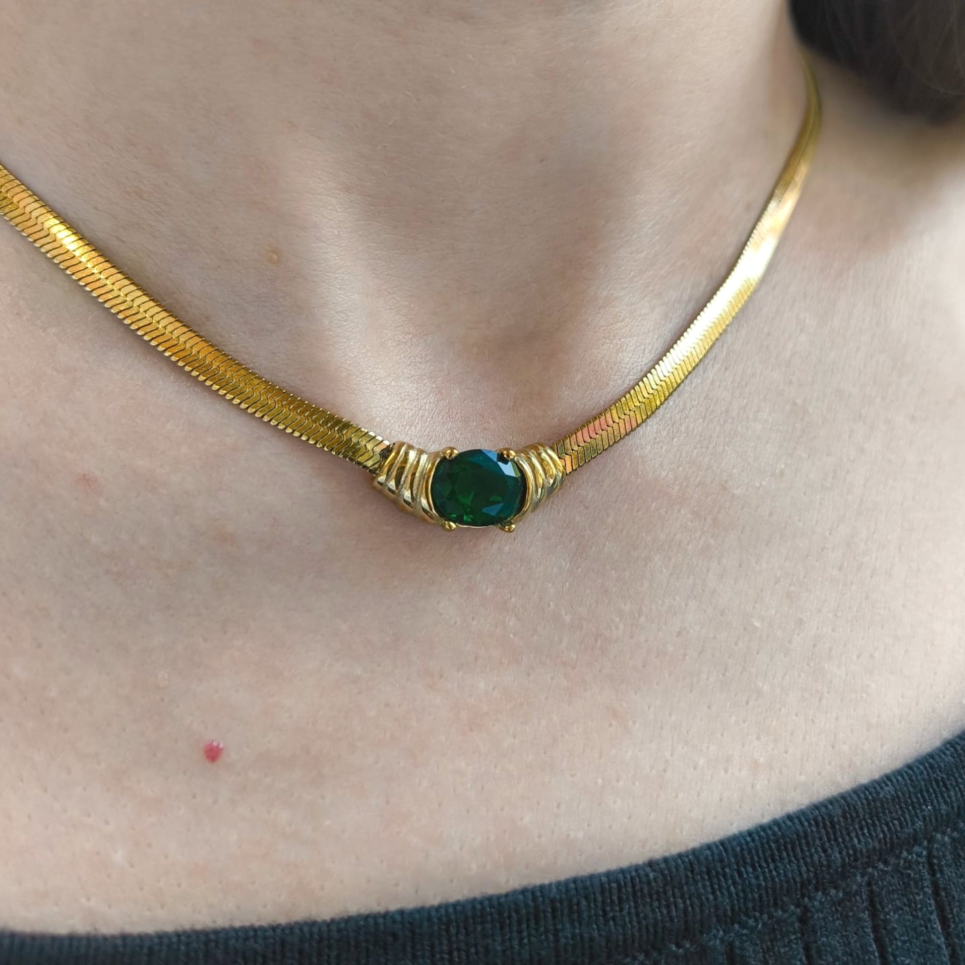 Gold necklace with a green gemstone on a person's neck
