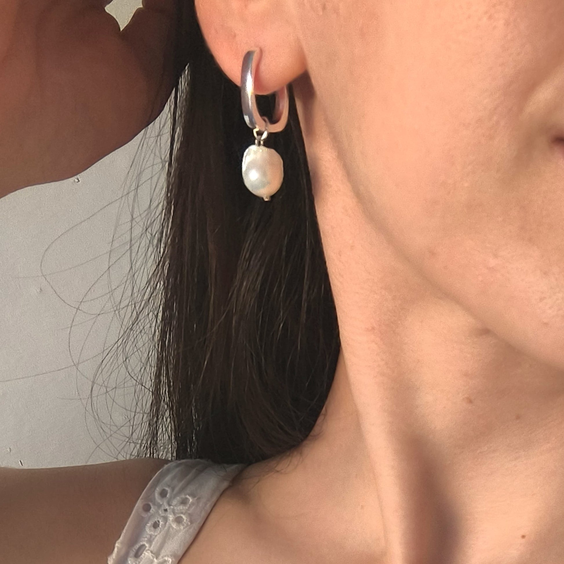 Close-up of a person wearing a silver hoop earring with a pearl pendant.