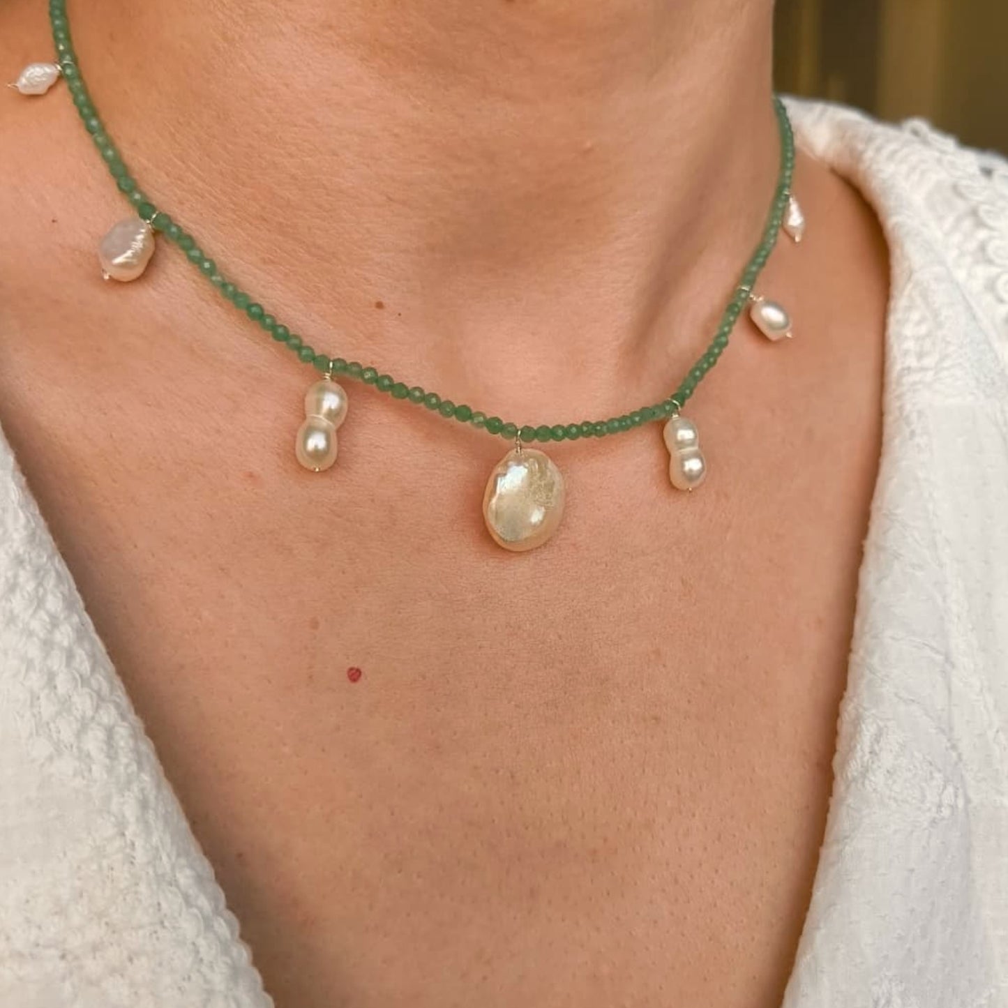 Necklace with green beads and pearls on a person wearing a white textured garment.