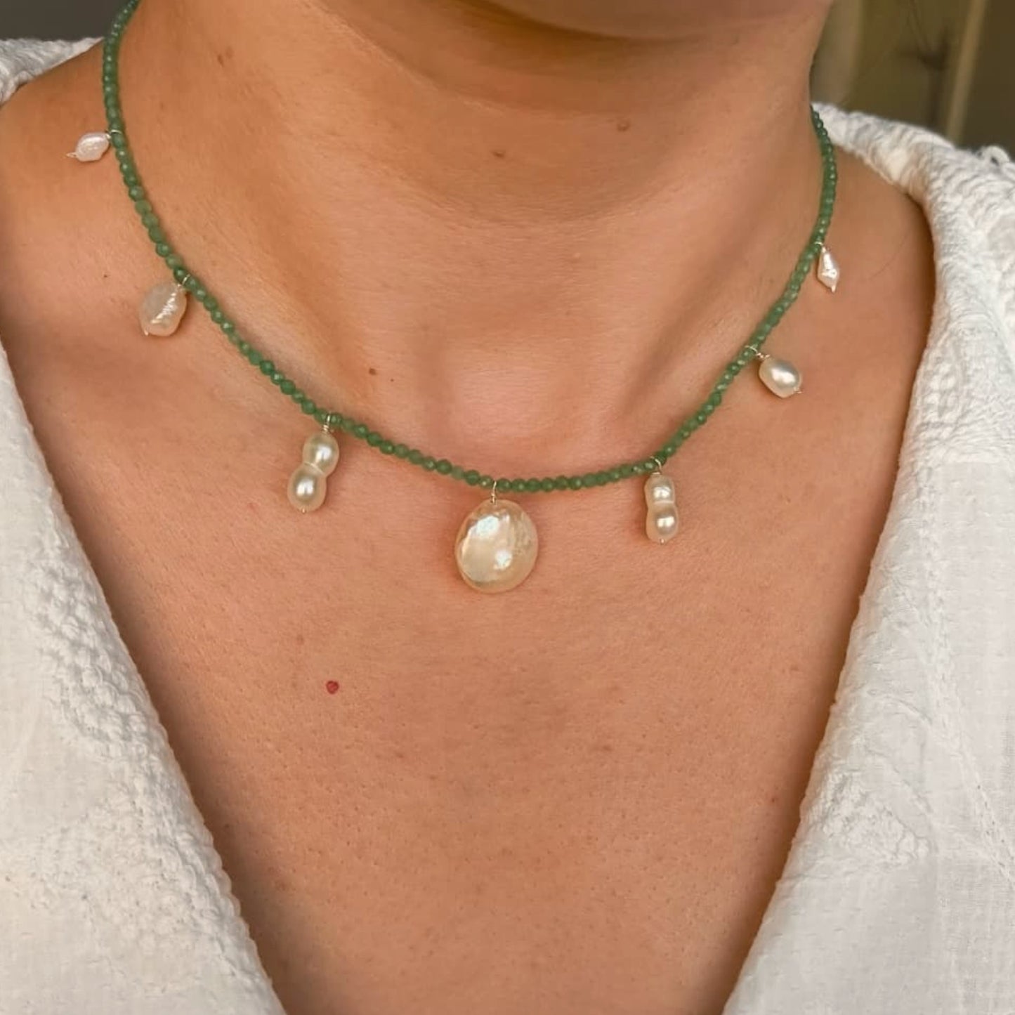 Close-up of a green beaded necklace with pearl-like pendants on a person wearing a white top.