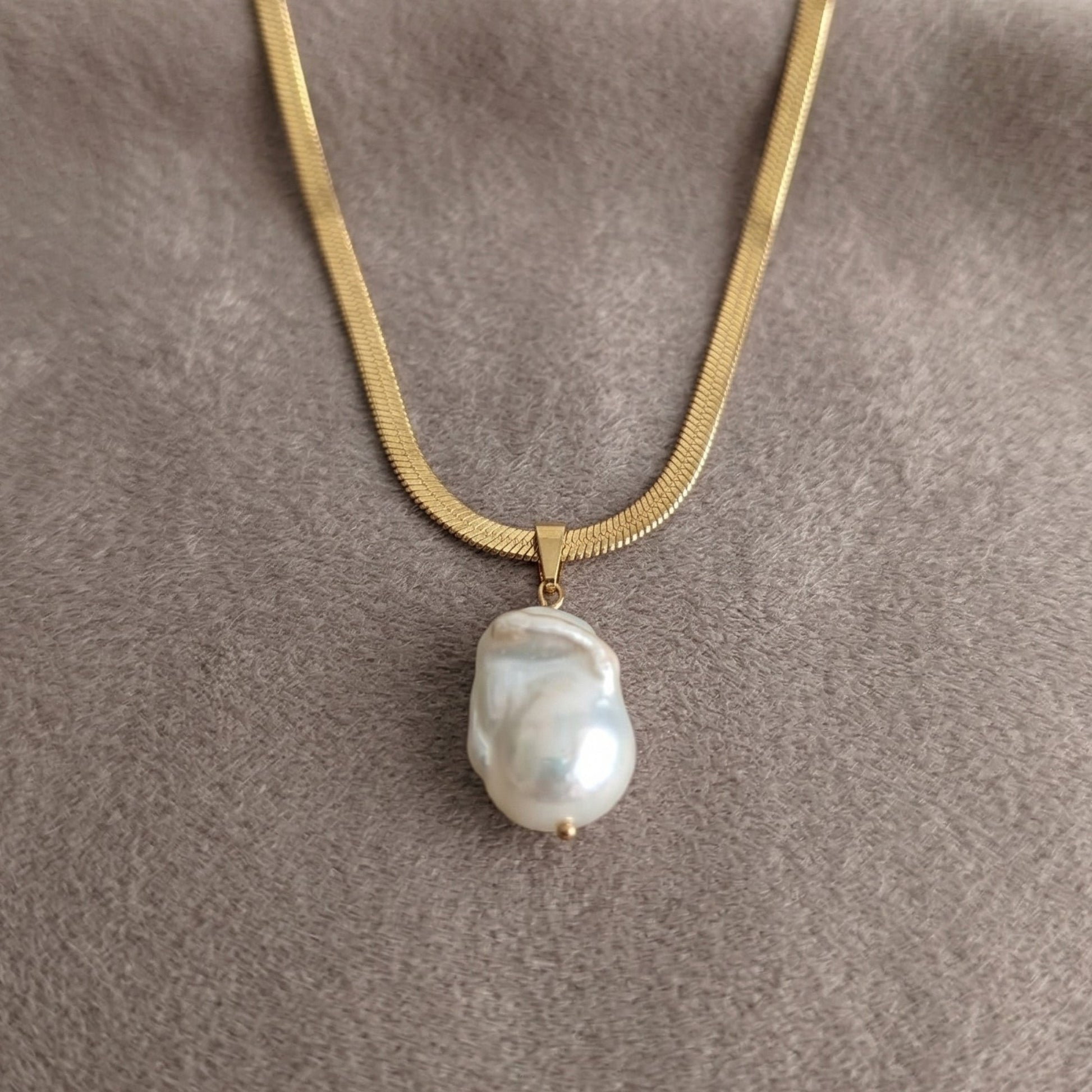 Gold necklace with a baroque pearl pendant on a gray background