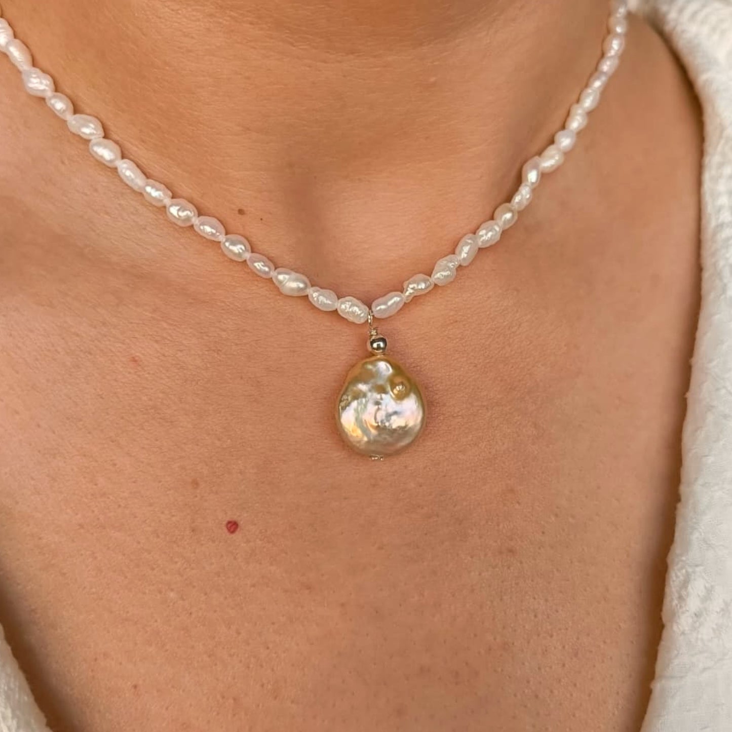 Pearl necklace with a large pearl pendant on a person's neck