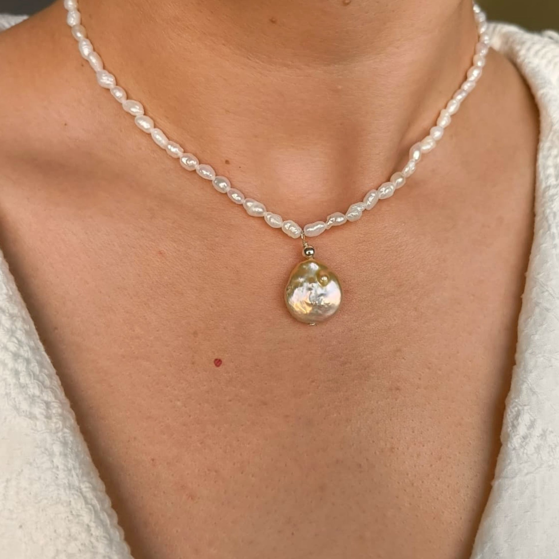 Pearl necklace with a large pendant on a person wearing a white top.