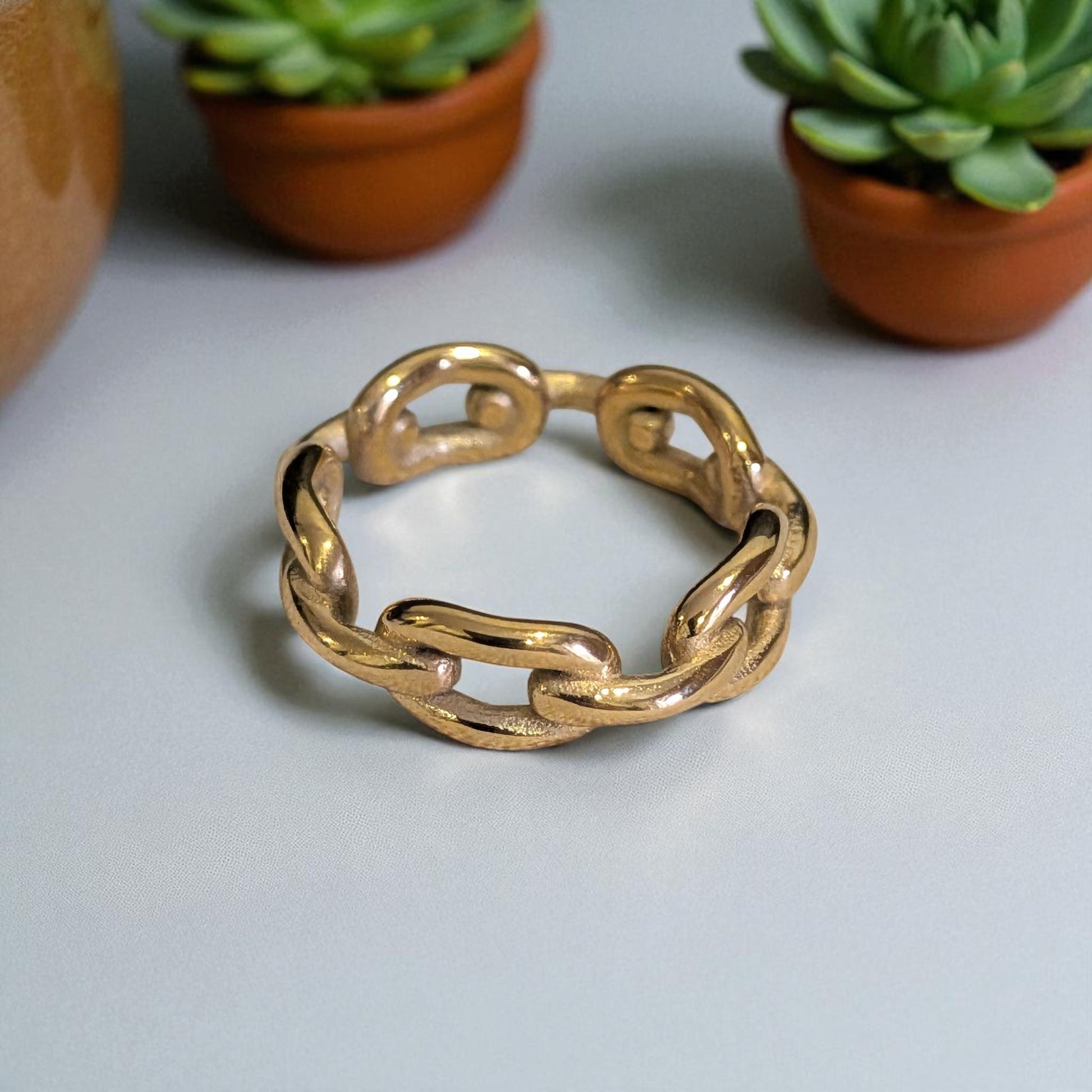 18k Gold plated chain-style ring on a light gray surface with potted plants in the background