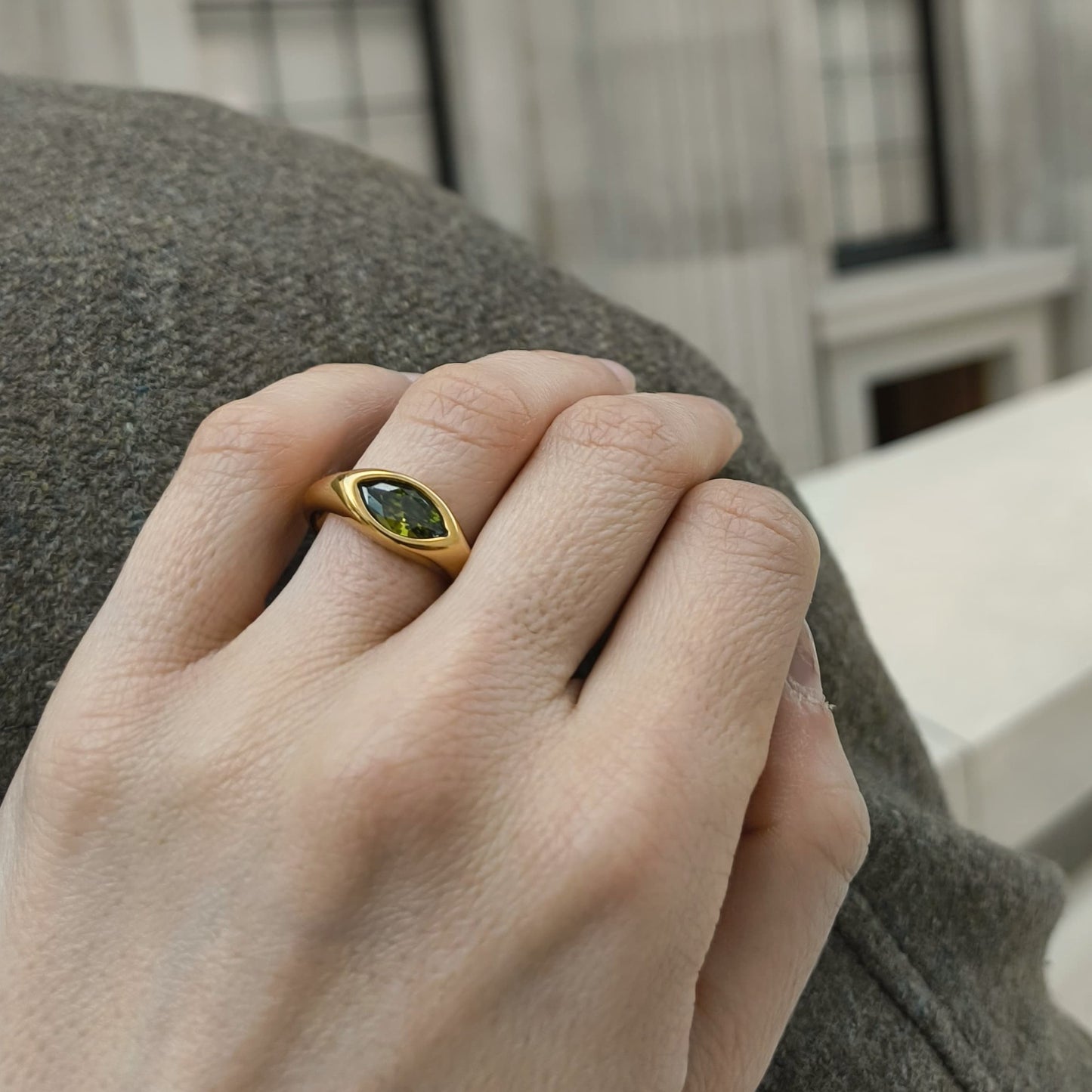 Hand wearing a gold ring with a green gemstone, blurred background