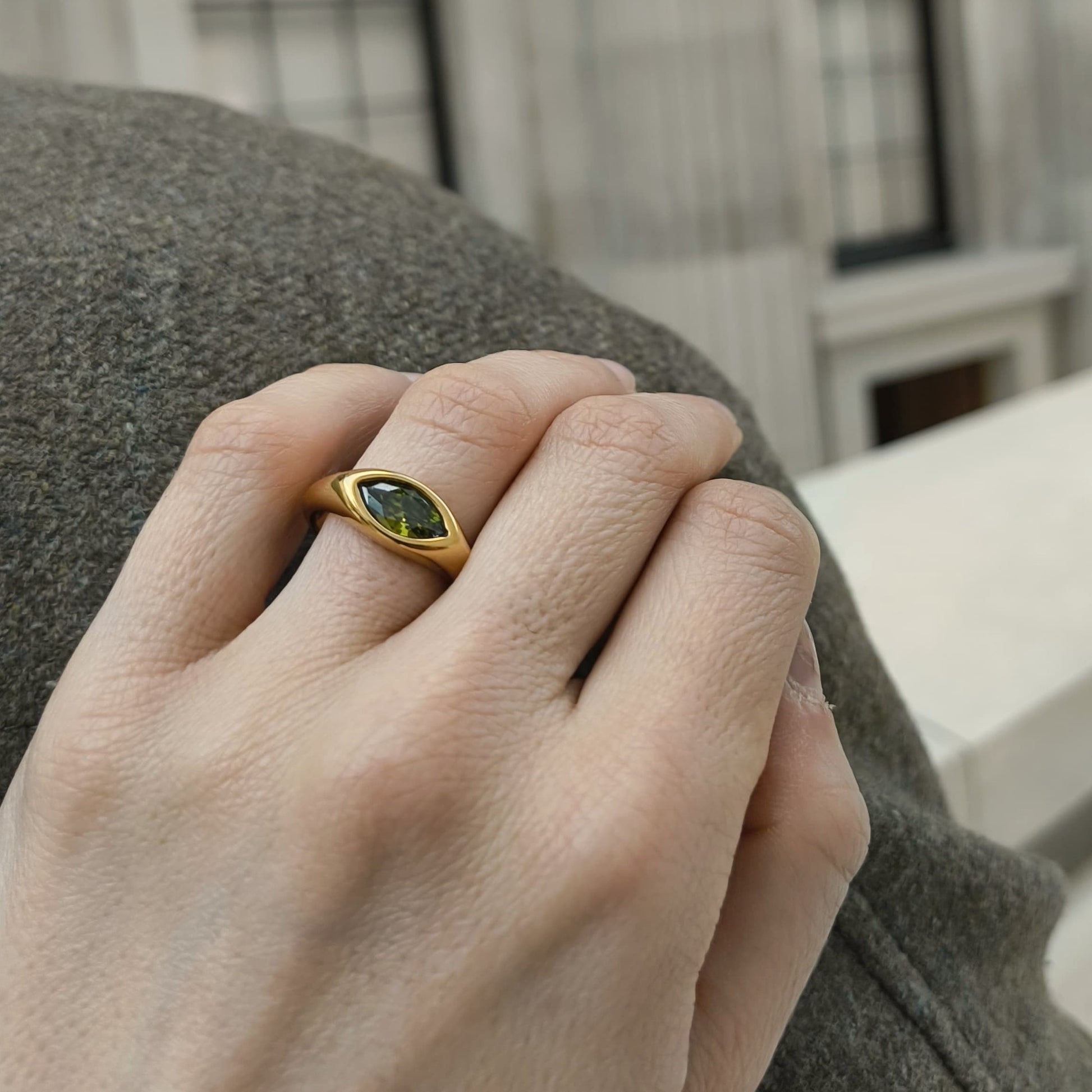 Hand wearing a gold ring with a green gemstone, blurred background