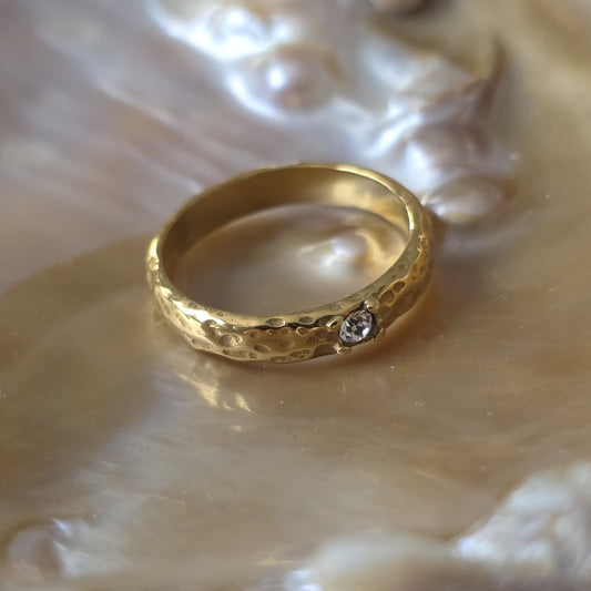 Gold ring with a diamond on a textured beige surface
