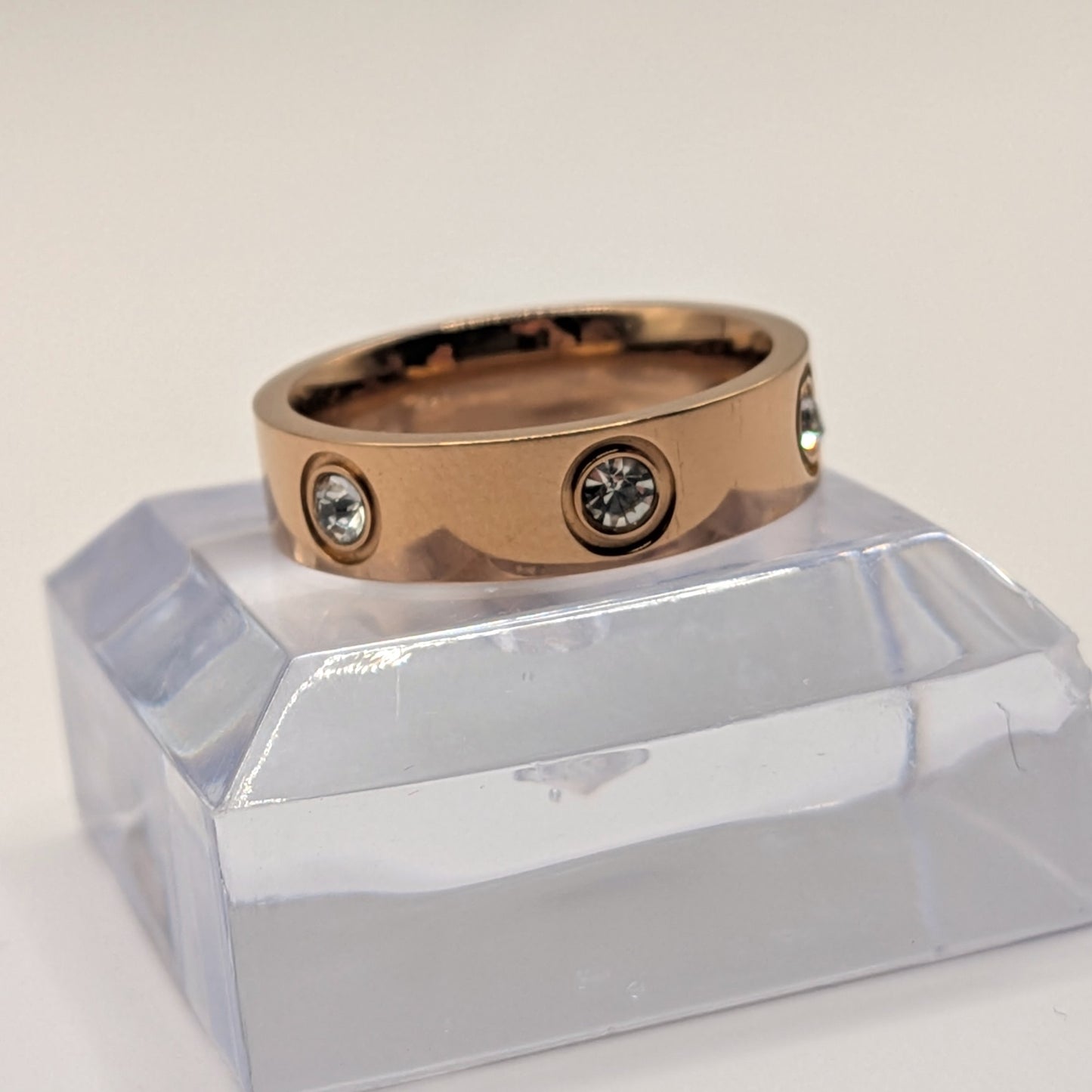 Rose gold ring with embedded diamonds on a clear stand against a light background