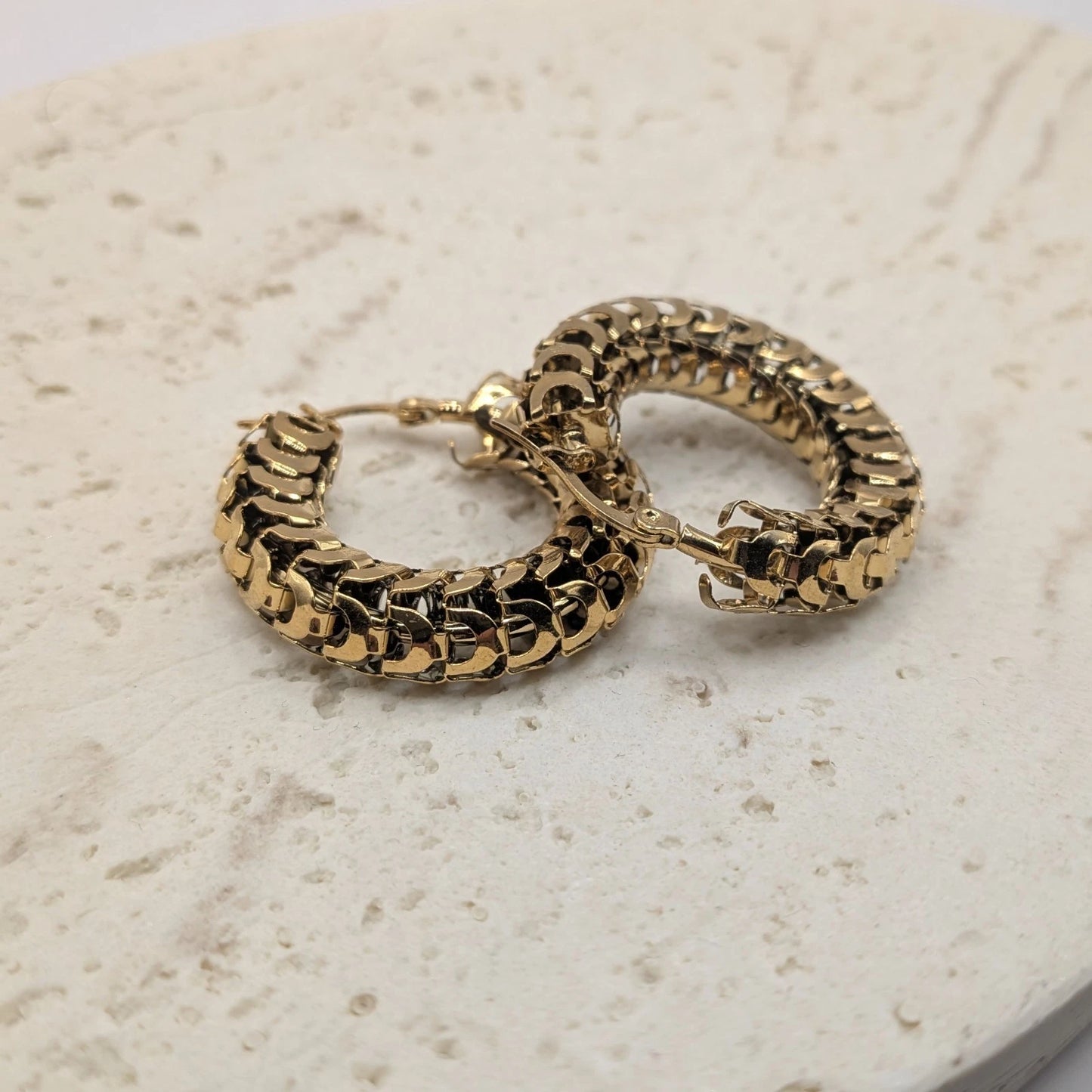 Gold hoop earrings on a textured beige surface