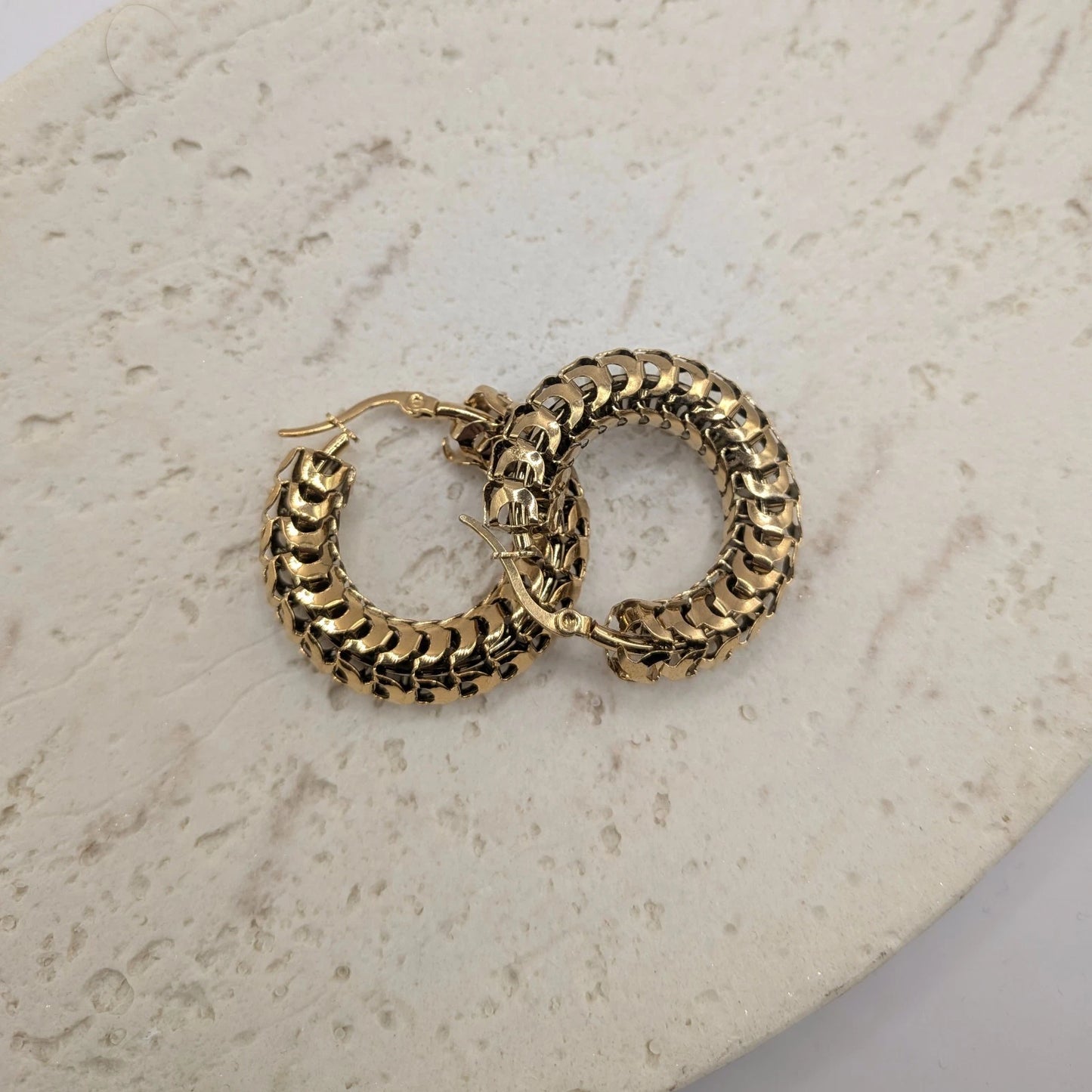 Gold hoop earrings on a light stone surface