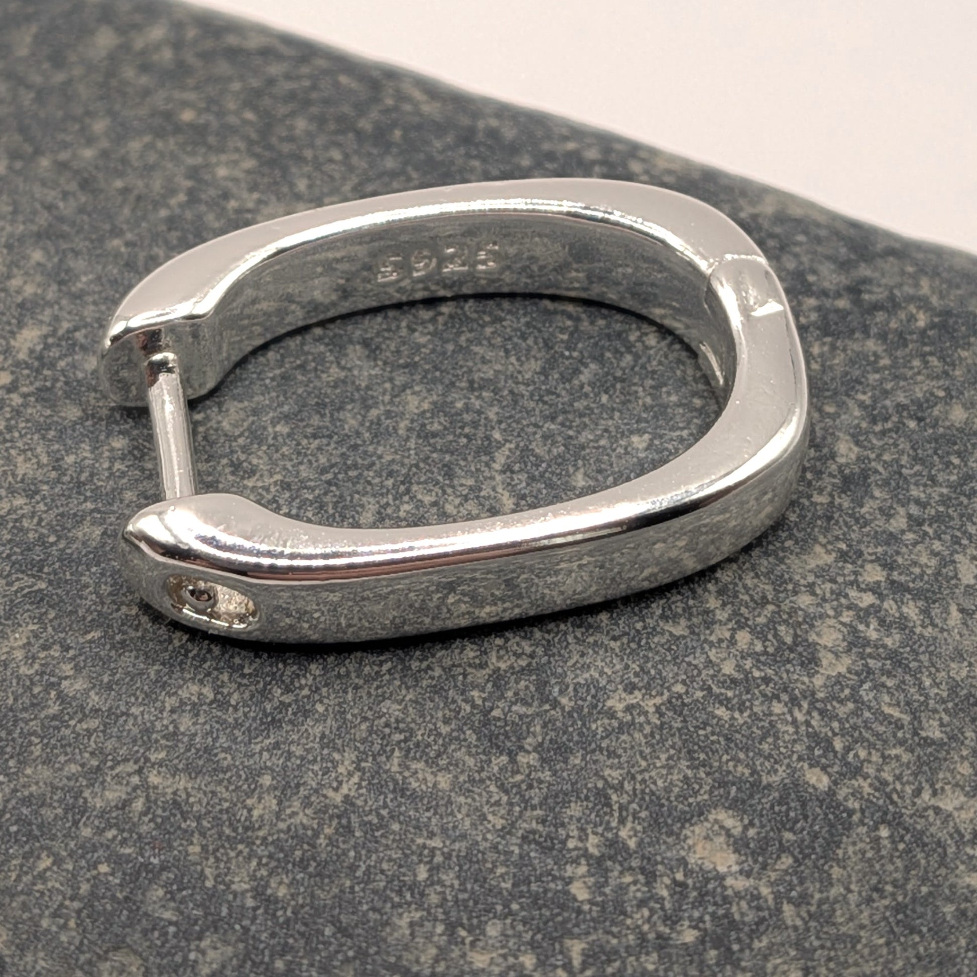 Silver hoop earring on a dark stone surface