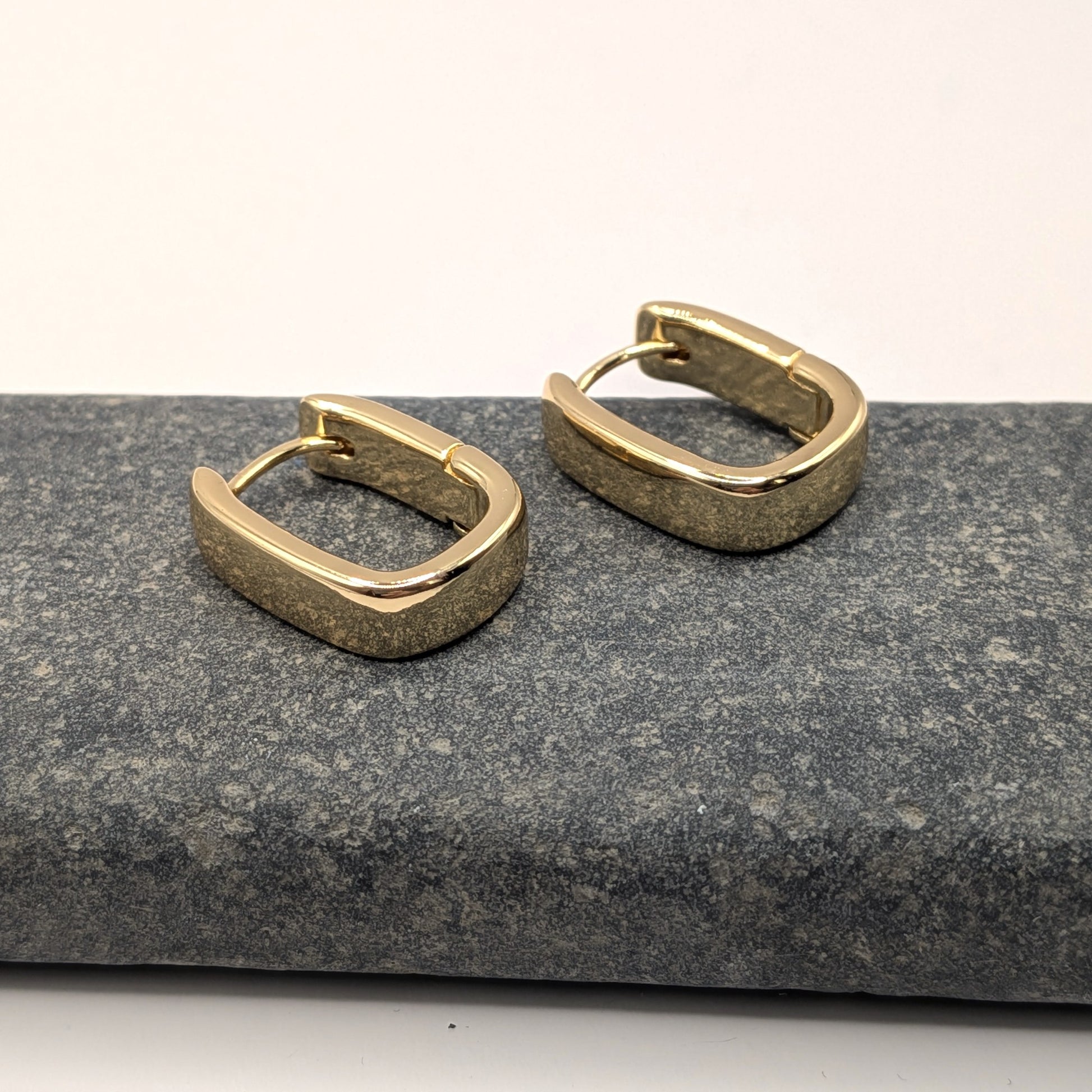 Gold hoop earrings on stone surface.