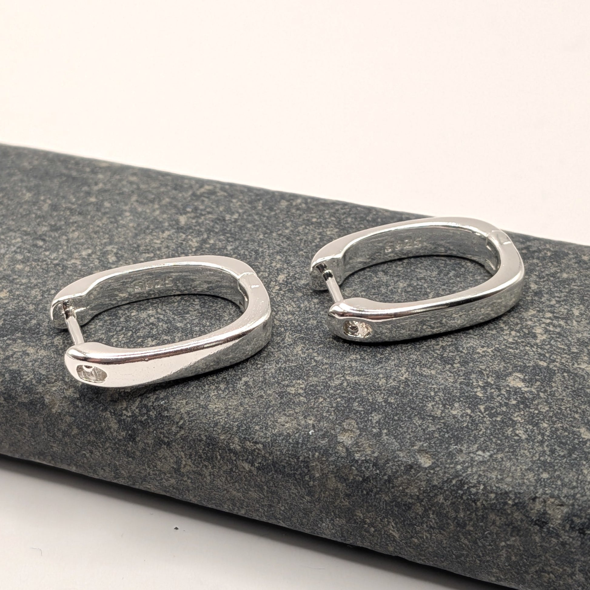 Pair of silver hoop earrings on a gray stone surface