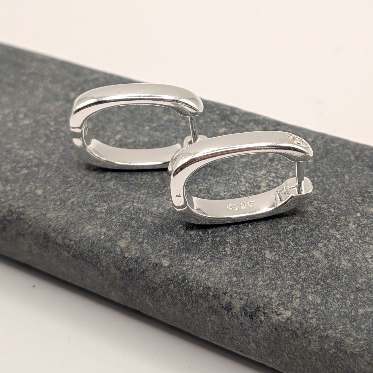 Pair of silver hoop earrings on a gray stone surface