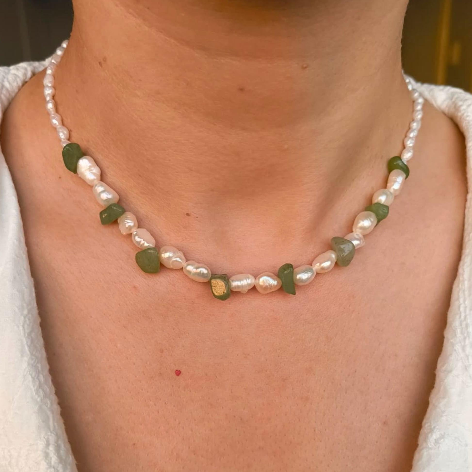 Pearl and green stone necklace on a person wearing a white top.