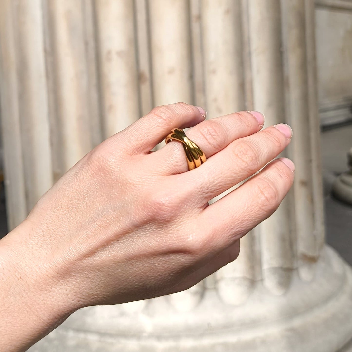 Hand wearing a gold ring with a blurred architectural background