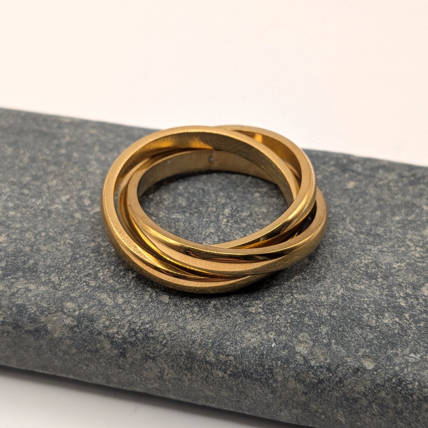 Gold ring with three interlocking bands on a gray stone surface