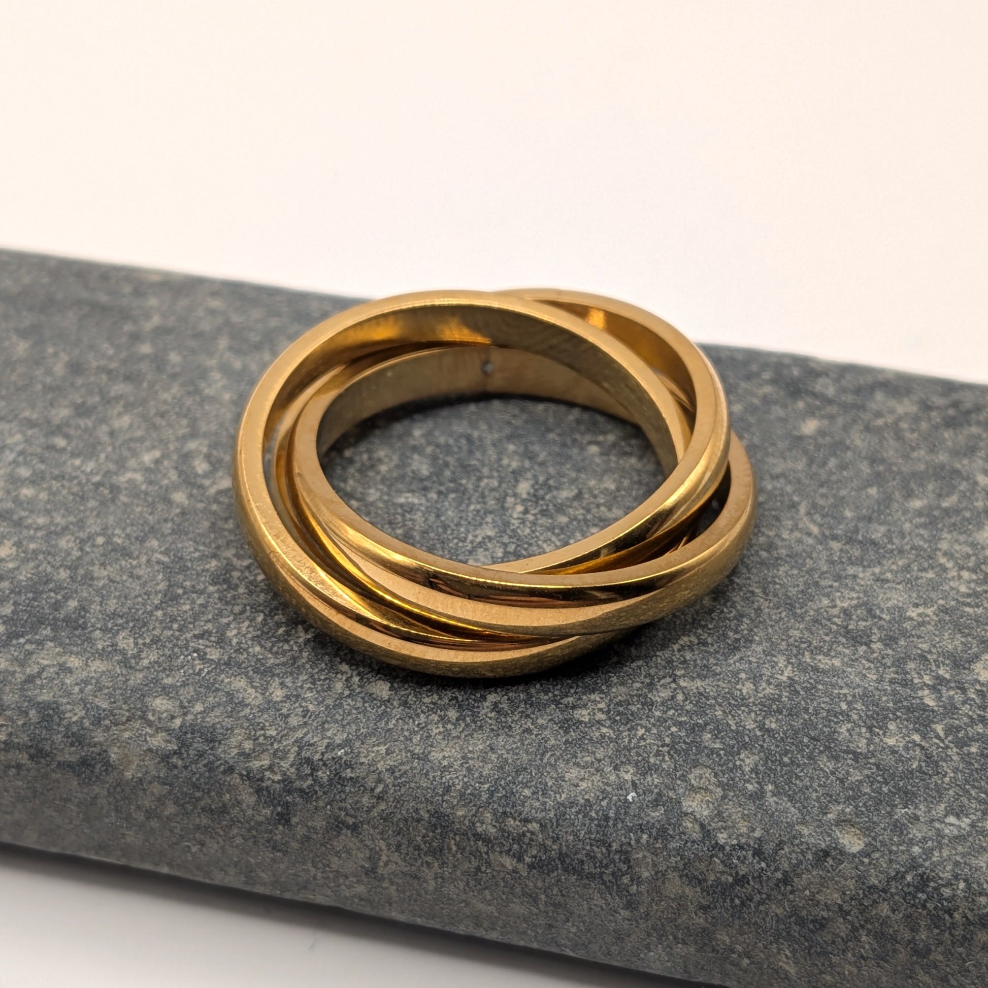 Gold ring with three interlocking bands on a gray stone surface
