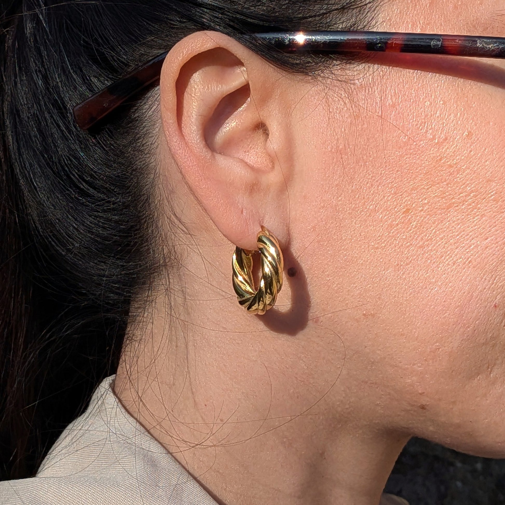 Close-up of an ear wearing a gold hoop earring with glasses on.