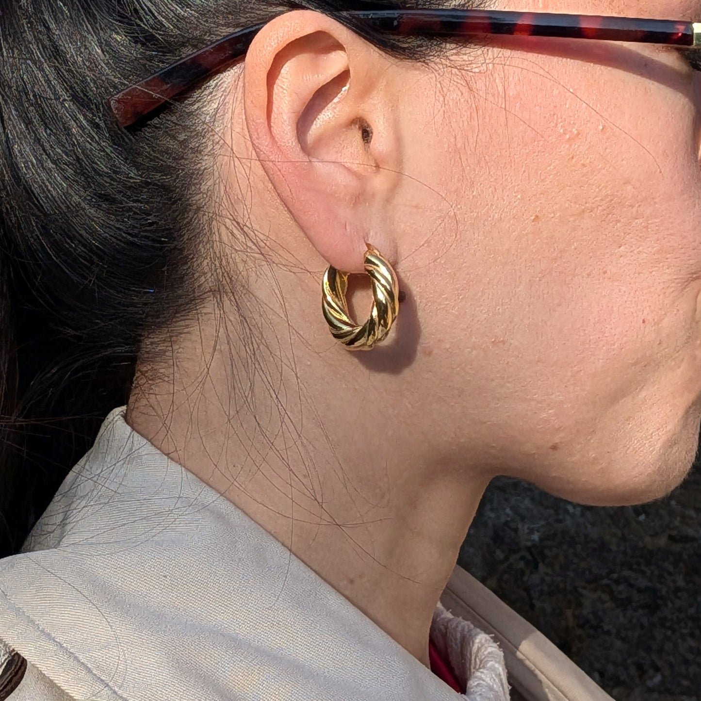 Close-up of a person wearing gold hoop earrings with sunglasses on.