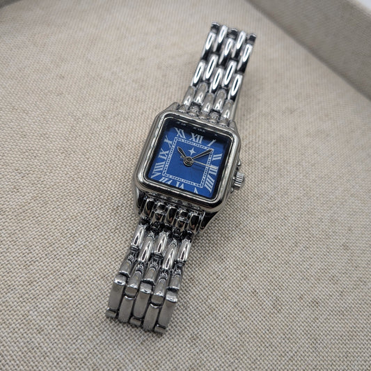 Silver watch with a blue face on a textured gray surface