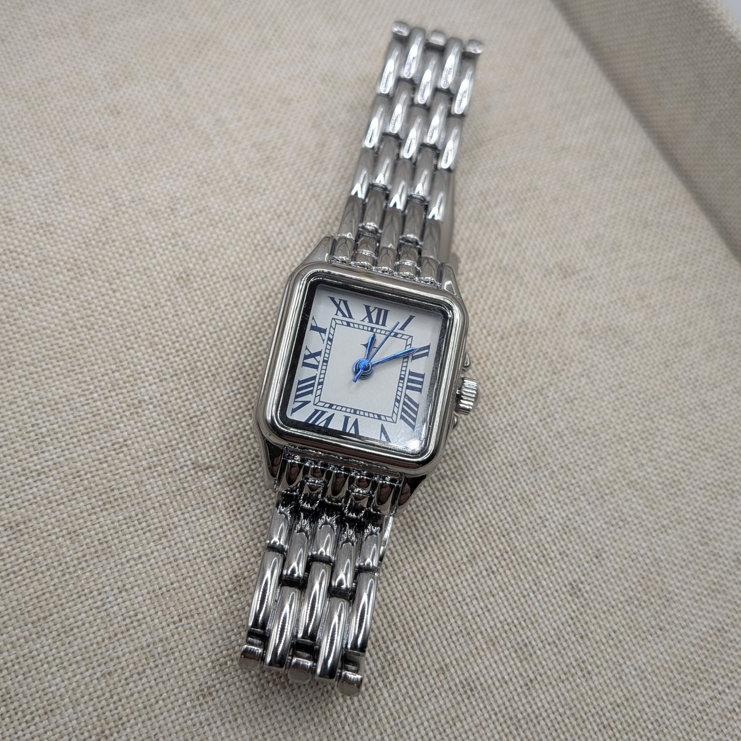 Silver watch with a chain strap on a beige fabric background